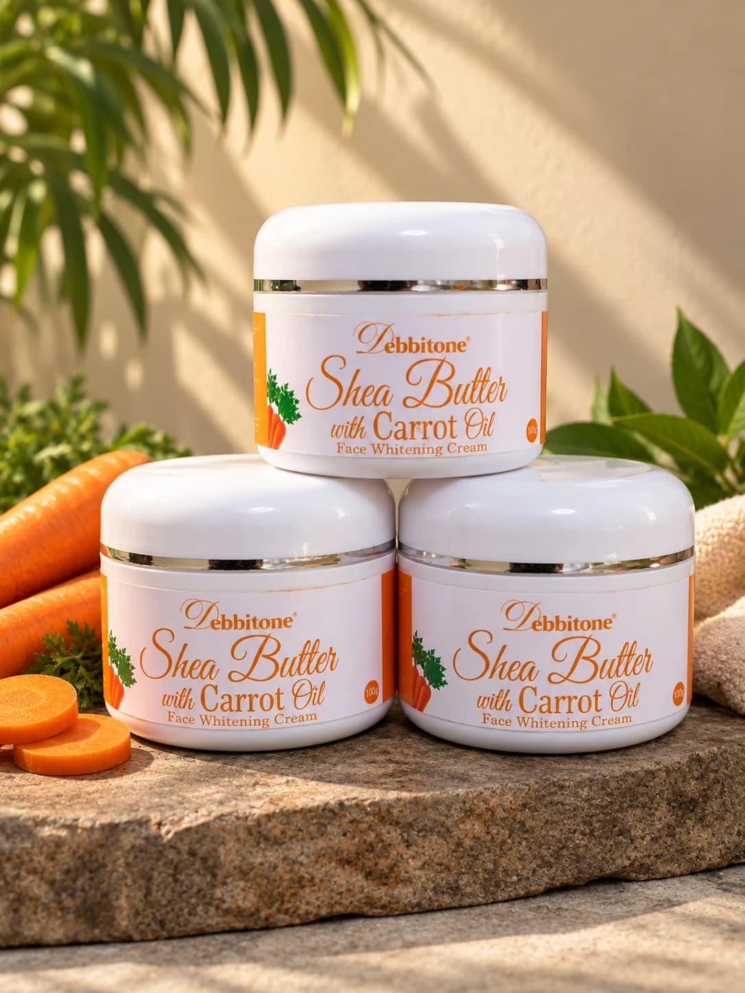 Jars of Debbitone SheaButter Carrot Brightening Cream stacked beside sliced carrots
