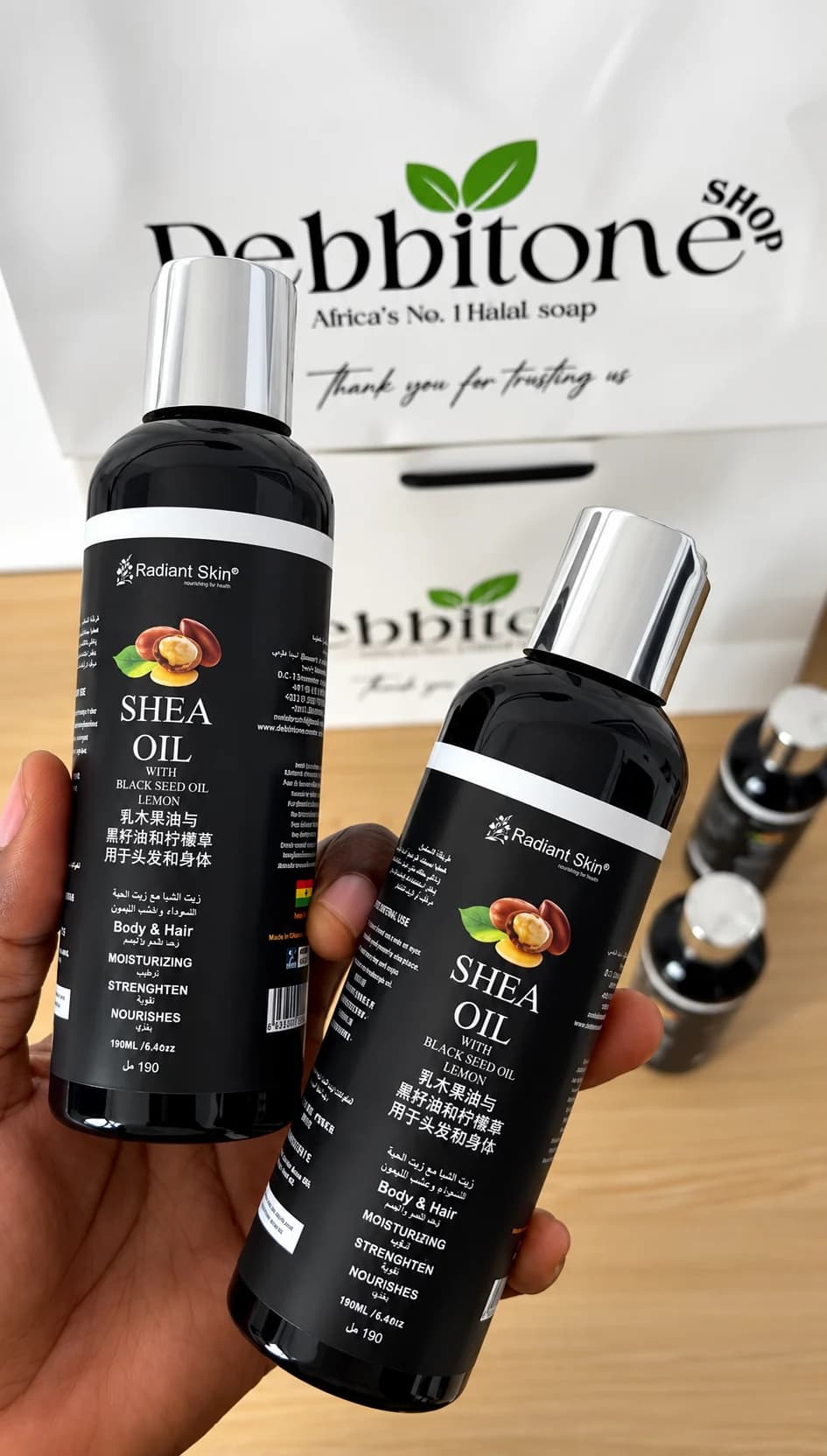 Two bottles of Debbitone Brightening Shea Oil held in front of a Debbitone Shop bag